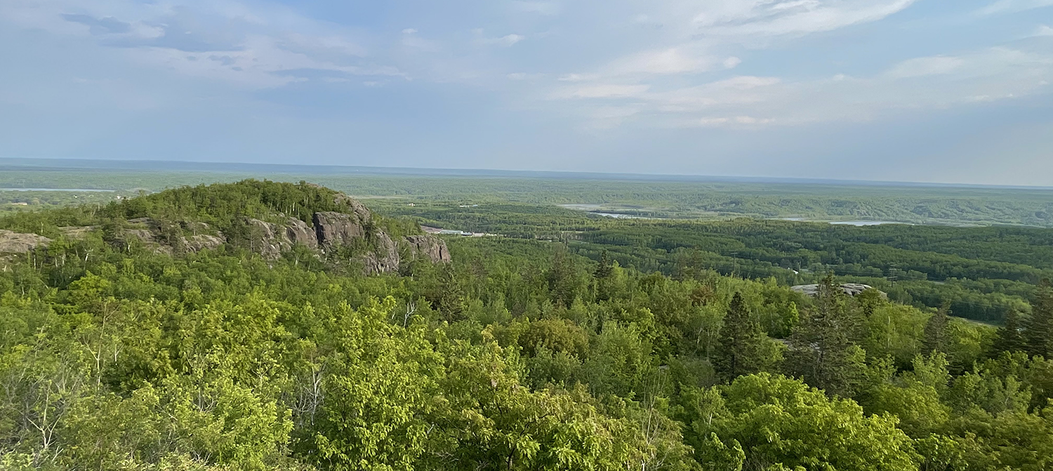 photo from a hilltop west of duluth showing blue sky, green tree tops, rocky outcrops and saint louis river