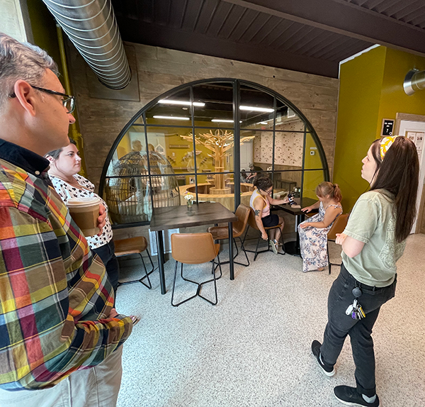 northland foundation staff members michael colclough and amanda vuicich stand in a bright indoor area listening to misha smith talking. They are just outside the cat lounge and there is a large arched window into the lounge. two people sit at a table outside the window waiting for their turn to enter the lounge.