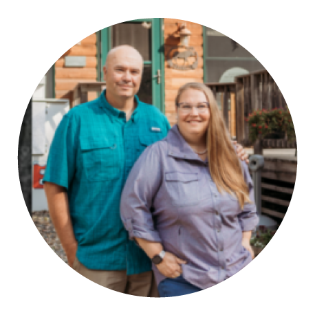 preston and aimee osborne stand smiling in front of a log lodge building with a deck and an outdoor ice cooler 