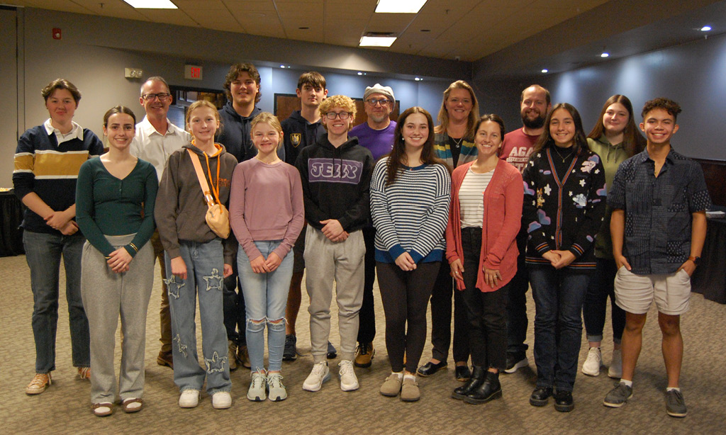 group photo of 11 of the 12 YIP board members and all 5 of the adult representatives. They are in a standing in a meeting space and smiling.